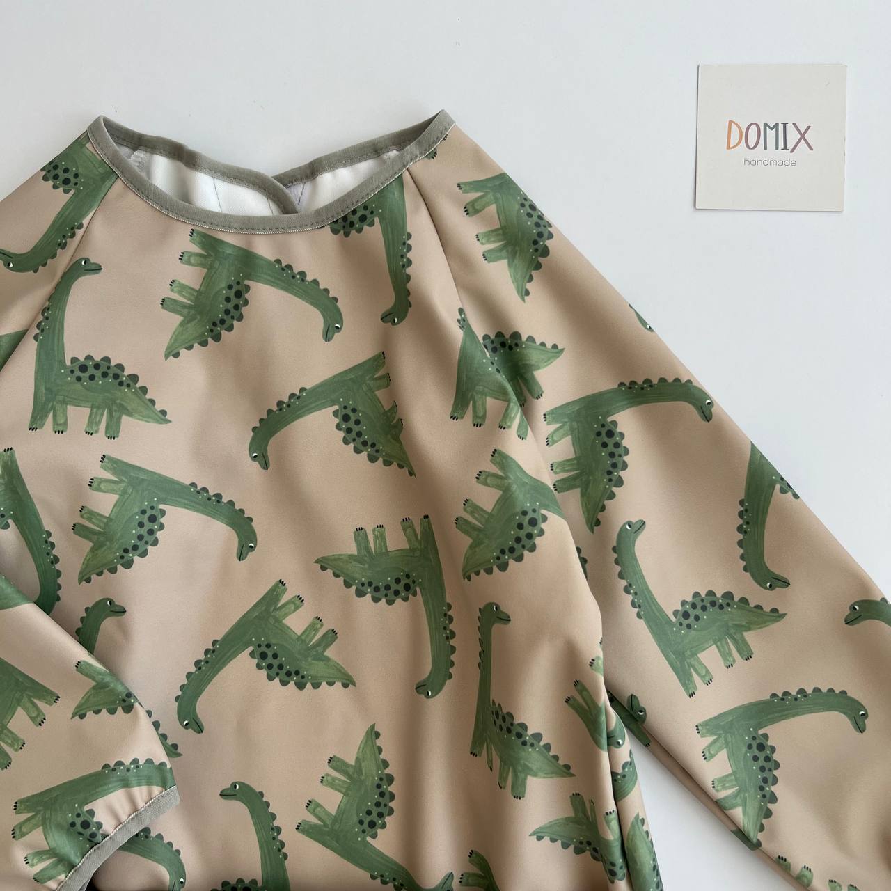 Fabric with green dinosaur pattern on beige background, DOMIX brand visible