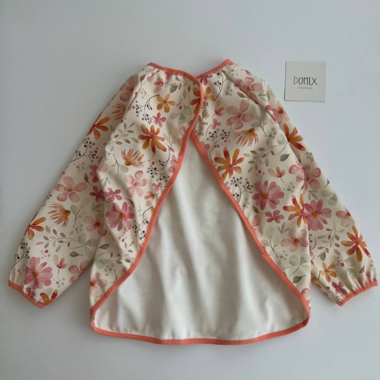 Floral-patterned baby jacket on a white background with a brand label.
