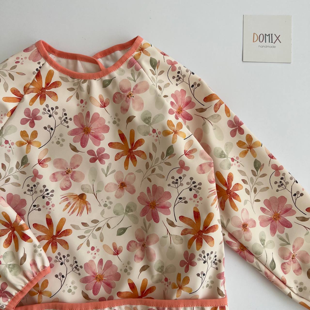 Floral-patterned long-sleeve shirt with orange trim on a white background, featuring the brand 'DOMIX'.